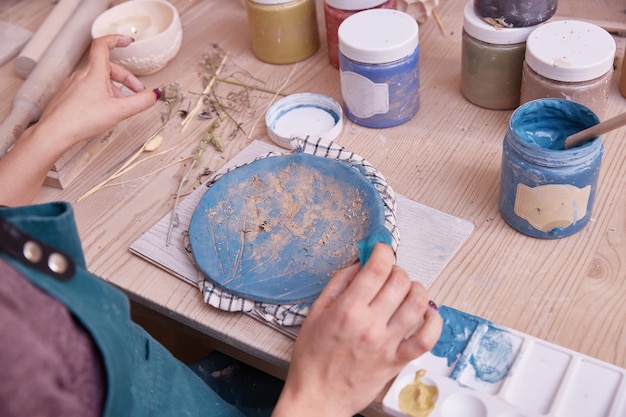 Professional potter works on painting plates in the workshop Woman Ceramist paints a plate with blue color