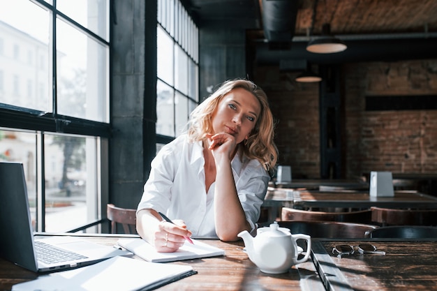 Professional psychologist is ready to help you. Businesswoman with curly blonde hair indoors in cafe at daytime.