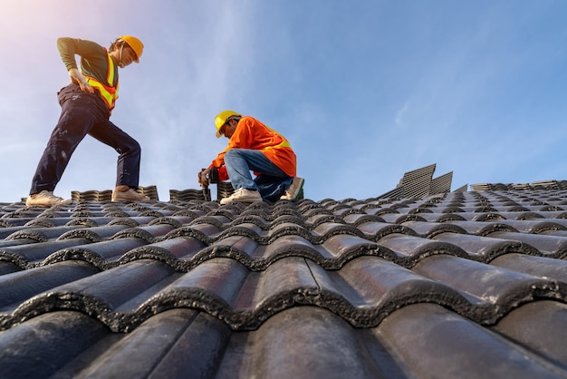 Professional and qualified roofer in protective uniform wear use electric drill to install the Concrete Roof Tiles on the new roof of new modern building construction