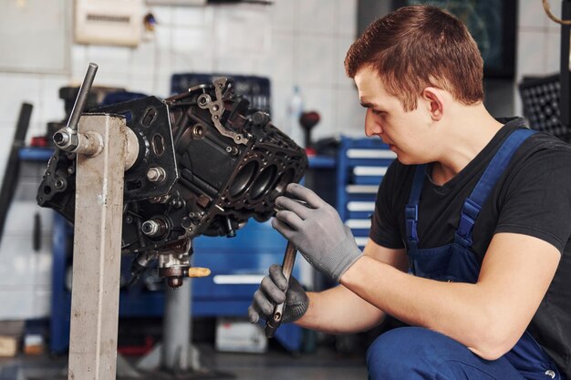 Professional repairman in garage works with broken automobile engine