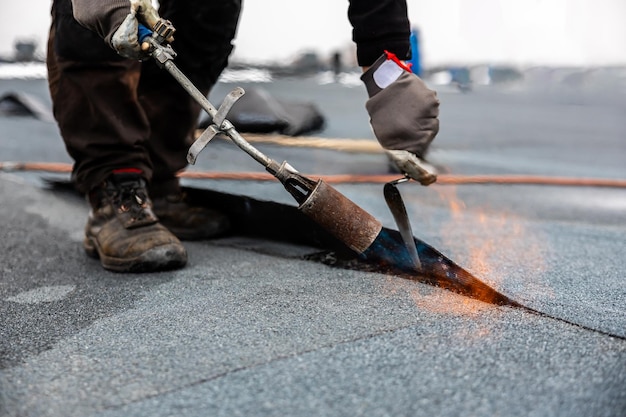 professional roofer applying bitumen roll on flat roof with a gas burner at a modern construction site