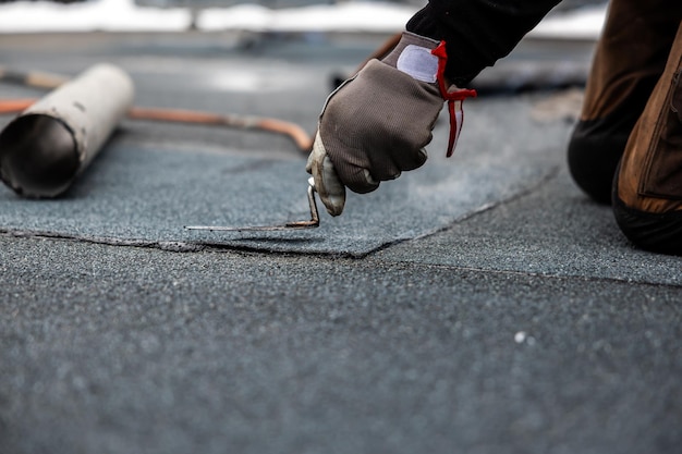 professional roofer applying bitumen roll on flat roof with a gas burner at a modern construction site