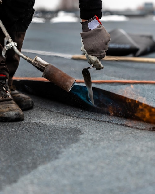 professional roofer applying bitumen roll on flat roof with a gas burner at a modern construction site