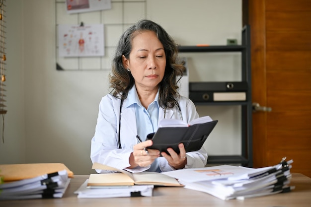 Professional senior Asian female doctor at her office desk checking her surgery schedule