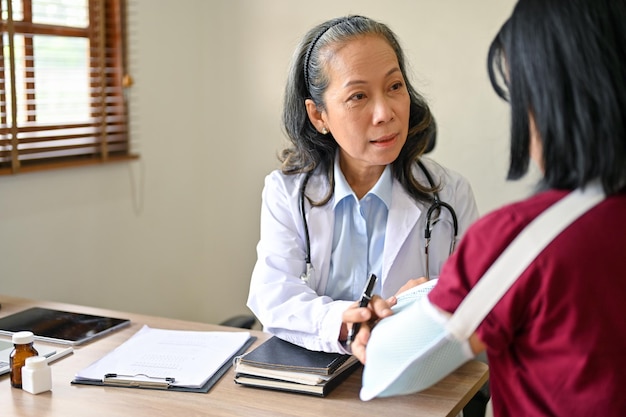 A professional senior Asian female orthopedic doctor consulting a surgery plan with a patient