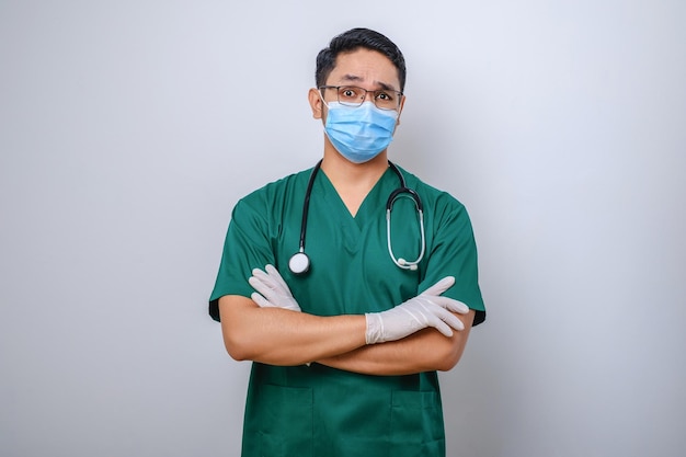 Professional seriouslooking asian doctor medical worker in stethoscope and scrubs wearing medical mask doing cross arms