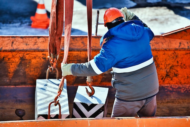 Professional slinger in construction helmet at factory unloads cargo Loading training