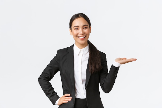 Professional smiling businesswoman introduce her project during meeting. Saleswoman in black suit holding hand right as showing product, holding on palm over blank white background