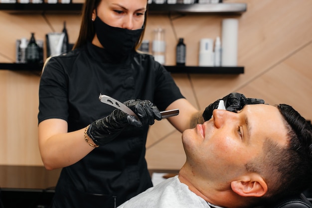 Professional stylist in a modern stylish barbershop shaves and cuts a young man's hair