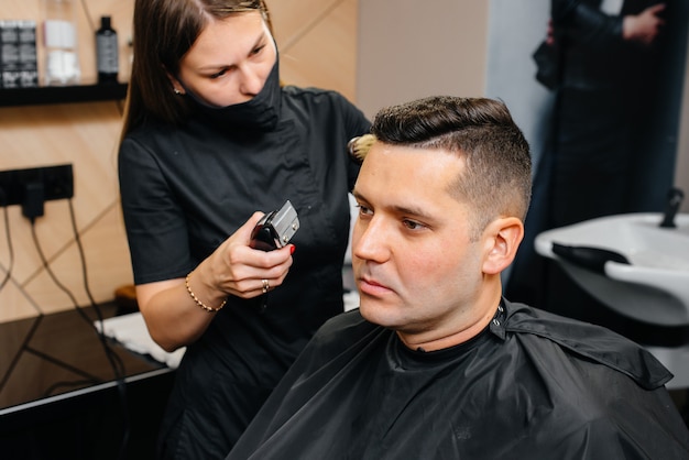 Professional stylist in a modern stylish barbershop shaves and cuts a young man's hair