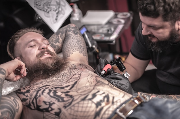 Professional tattoo artist does tattoo on the skin of his client in tattoo studio.