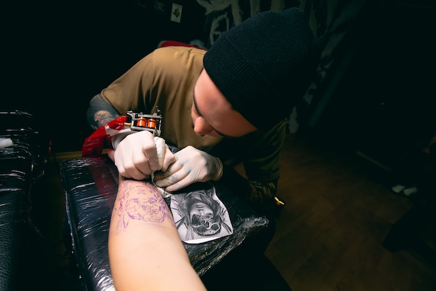 Professional tattoo artist makes a tattoo on the client hand closeup