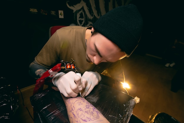 Professional tattoo artist makes a tattoo on the client's arm