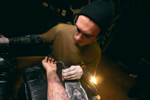 Professional tattoo artist makes a tattoo on the client's hand close-up