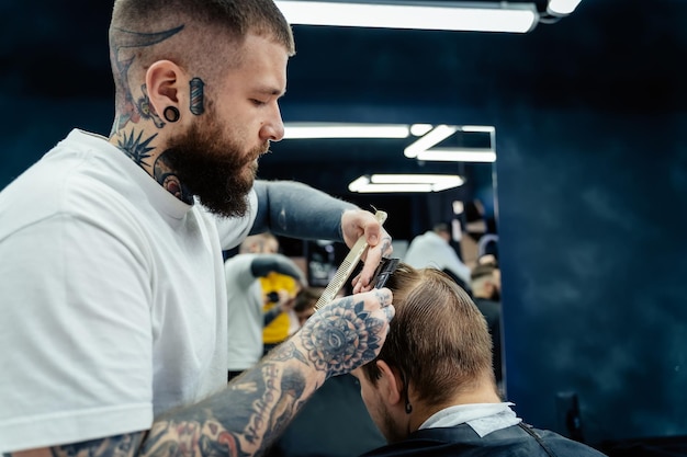 Professional tattooed barber using cutthroat razor cutting hair attractive male is getting a modern