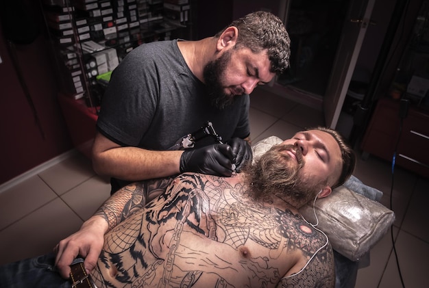 Professional tattooer working tattooing in tattoo parlorTattooist showing process of making a tattoo in tatoo salon