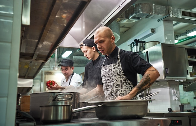 professional team of chef and two young assistants cooking in a restaurant kitchen