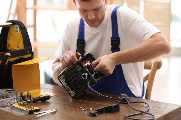 Professional technician repairing electric fan heater with screwdriver at table indoors