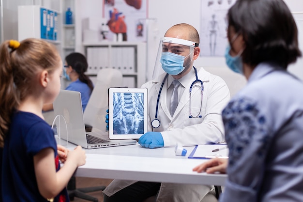 Professional therapeutist showing radiography on tablet pc during coronavirus pandemic