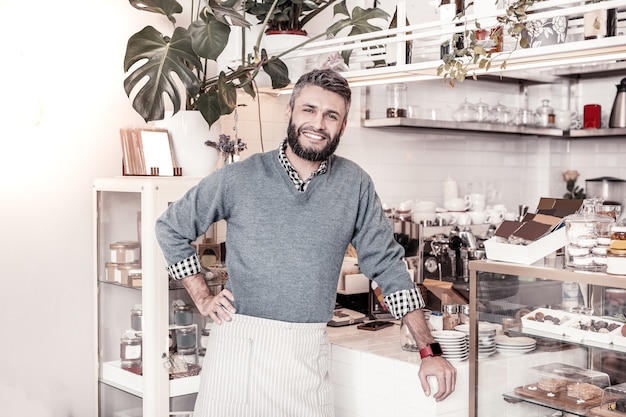 Professional waiter. Pleasant cheerful man standing in the bakery while working in the cafeteria