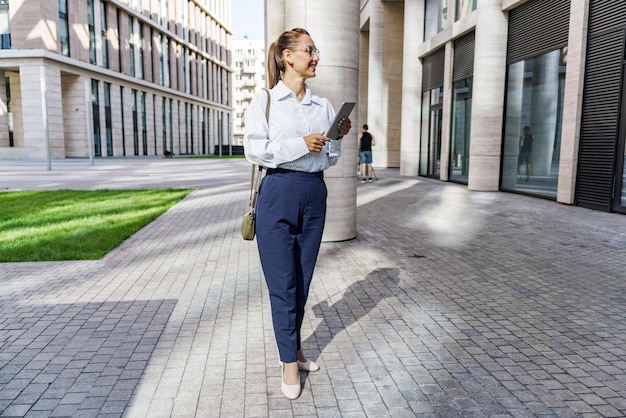 Photo professional woman walking with a tablet in a modern urban business district