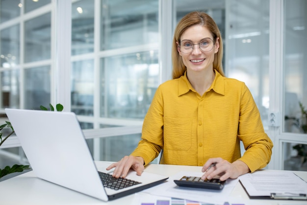 Photo professional woman working on laptop and using calculator in a bright modern office