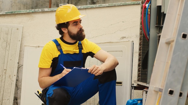 Professional worker comissioned by home owner to do air conditioner maintenance, checking internal parts. Expert repairman writing down cost of needed new components on clipboard