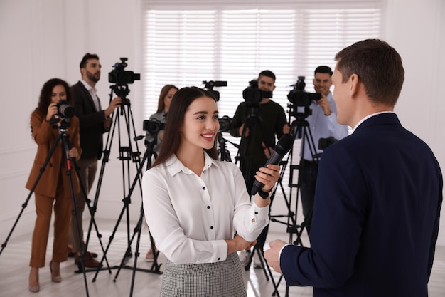 Professional young journalist interviewing businessman and group of video camera operators on background