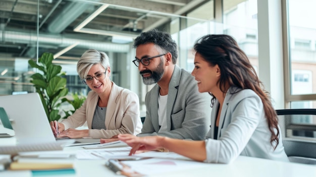 Professionals are smiling and engaging in a discussion around a laptop at a bright modern office table