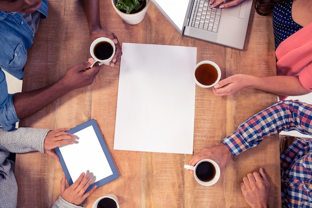 Professionals using technologies while holding coffee cups at desk