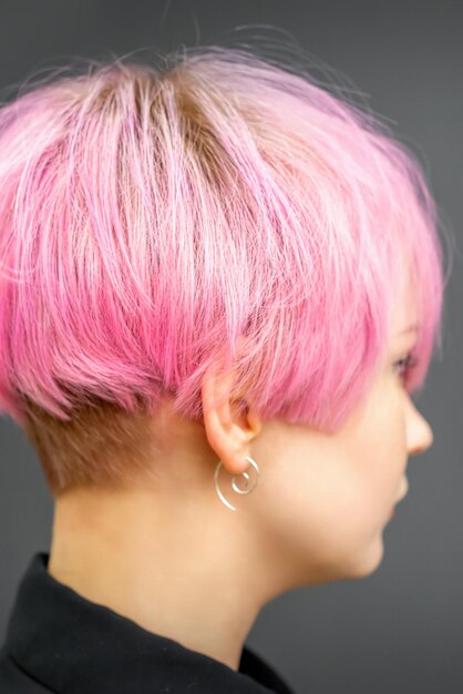 Profile of a beautiful young caucasian woman with short bob pink hairstyle on dark gray background