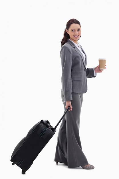 Profile of a businesswoman smiling with a suitcase and holding a coffee