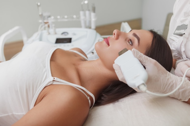 Profile close up of an attractive woman getting ultrasound facial cleanse by cosmetologist