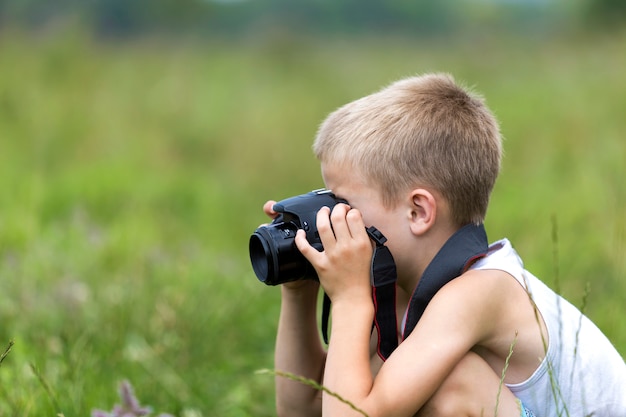 Profile close-up portrait of young blond cute handsome child boy with camera taking pictures outdoors on bright sunny spring.