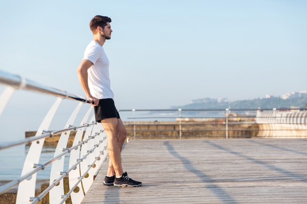 Profile of handsome young man standing on wooden terrace near the sea