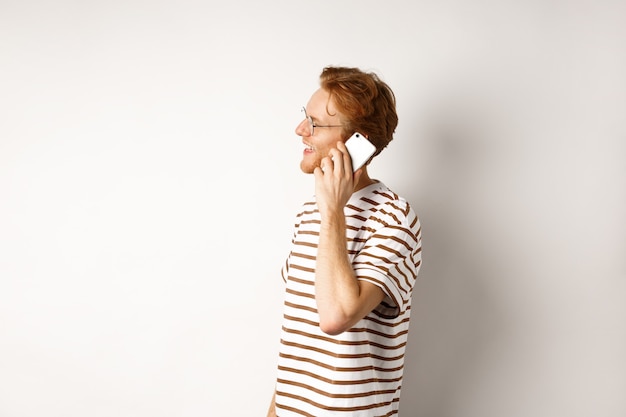 Profile of happy young handsome man talking on mobile phone, looking left and smiling, standing over white background