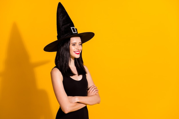 Profile photo of cute lovely young sorceress lady crossed arms look empty space beaming smiling role play event wear black headwear dress isolated bright yellow color background