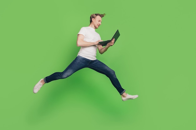 Profile photo of positive man hold computer jump run texting email wear white t-shirt on green color background