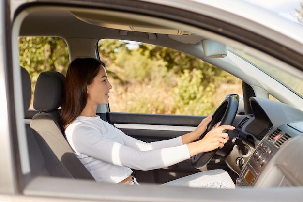 Profile portrait of delighted satisfied beautiful female with glad positive expression being satisfied with riding car alone sits on drivers seat looking at road with positive expression