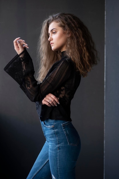 Profile portrait of a young woman dressed in a black suitcase and jeans over grey background