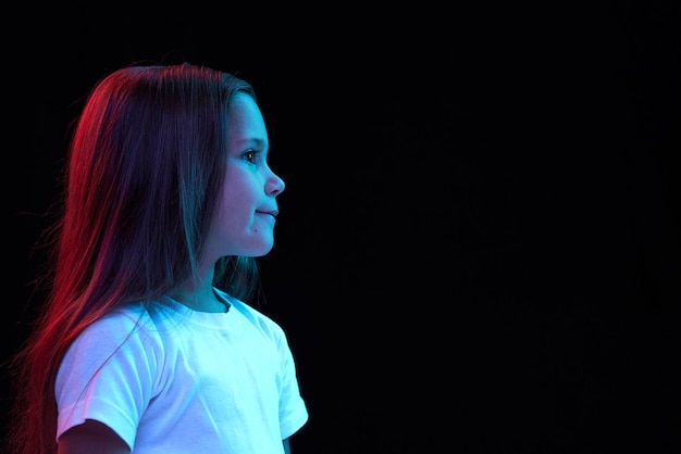 Profile view of little girl kid in white tshirt expressing emotions isolated over dark background