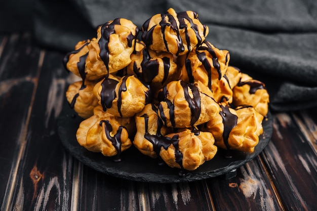 Profiteroles with chocolate cream on black plate