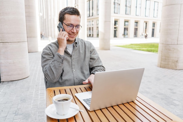 The programmer works in a cafe uses a phone and laptop summer time is outside