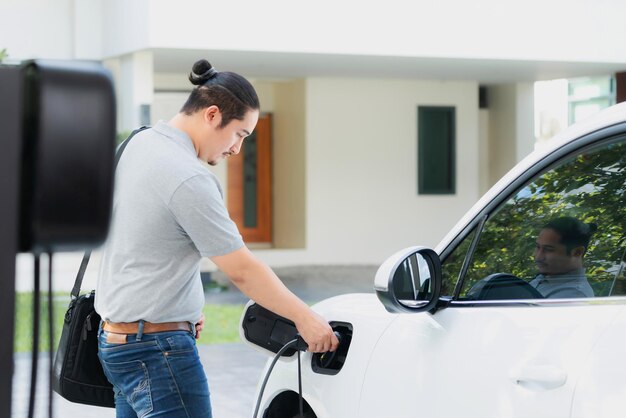 Progressive asian man recharge his EV car at home charging station