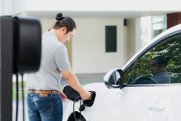 Progressive asian man recharge his EV car at home charging station