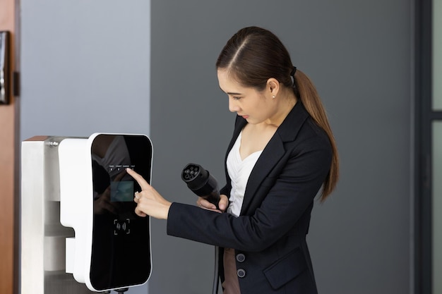 Progressive asian woman holding EV plug at home charging station