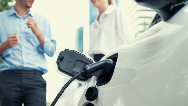 Progressive businessman and businesswoman install charger plug from charging station to electric car before driving around city center Eco friendly rechargeable car powered by clean energy