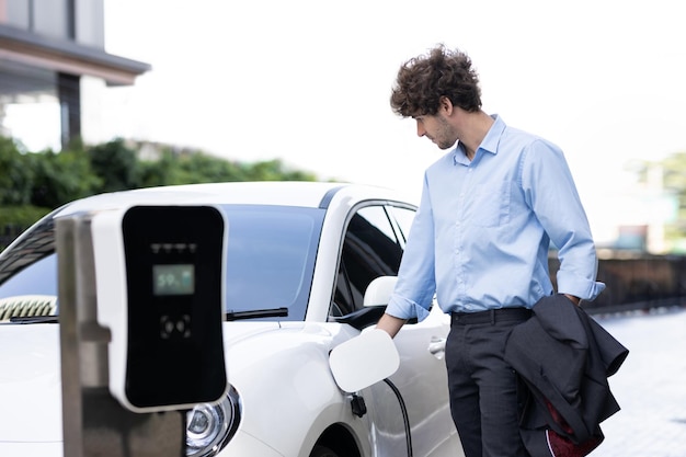 Progressive businessman plugs charger plug from charging station to EV