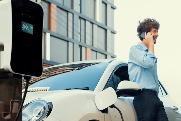 Progressive businessman talking on the phone with recharging electric vehicle