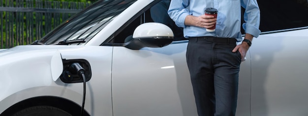 Progressive businessman with coffee and EV car at charging station